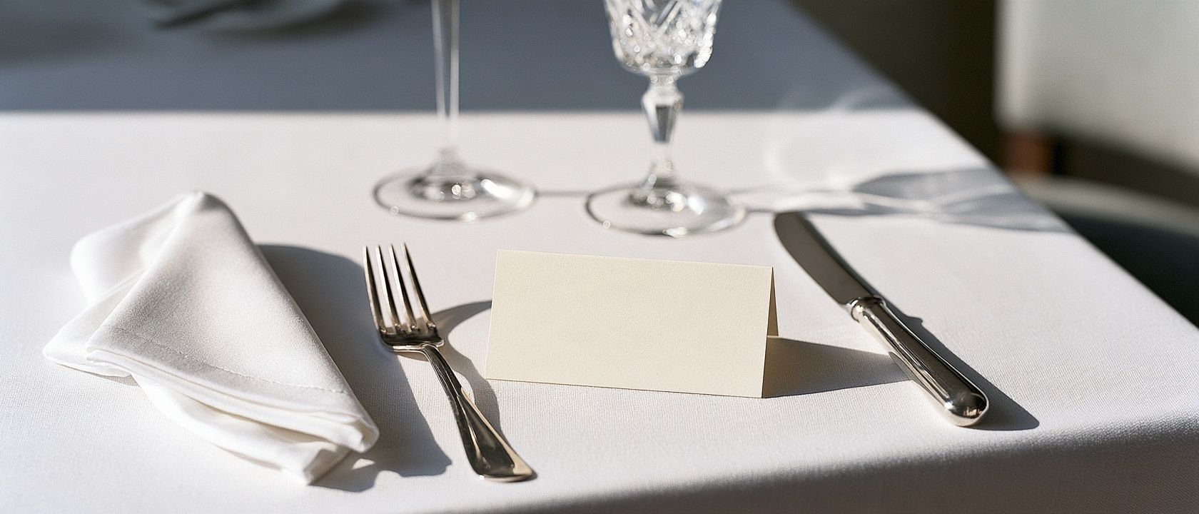 A place setting on white linen with silver cutlery and a blank place card